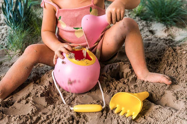 Child playing with pink sand toy and yellow shovel in the sand