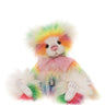 A plush teddy bear with fluffy white fur and vibrant rainbow-colored accents on its mane, ears, paws, and tail. The bear is wearing a pink bow tie and a silver bell, set against a solid white background.