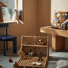 Wicker toy dollhouse with figurines on a carpeted floor in a room with wooden walls and a window.