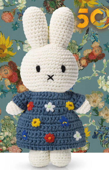 Crocheted bunny toy in a blue dress with floral patterns on a floral background