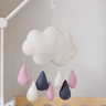 Cloud and raindrop mobile hanging above a crib with a plain background