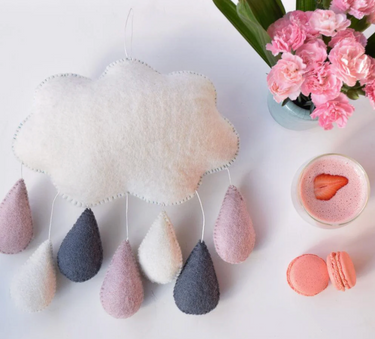 Decorative cloud with teardrop-shaped raindrops on a white surface with flowers and macarons.