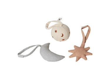 Three Ferm Living soft fabric baby accessories on a white background: a cream crescent moon with small brown star and moon details and a loop, a pale gray crescent moon with a loop, and a dusty pink starburst with a loop.