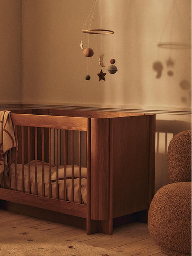 Wooden crib with a Ferm Living starry night mobile in a warm-toned nursery.