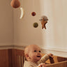 Baby in a crib with a Ferm Living mobile above, featuring stars and planets.
