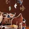 Children's room with Ferm Living hanging animal mobile, pillows, and toys on a wooden floor.