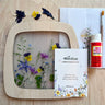 Pressed flowers in a wooden frame with Toverlux flower silhouette kit and Mod Podge on a wooden surface.