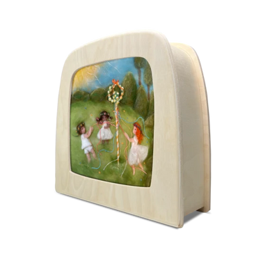 A lamp with a silhouette insert showing a colorful scene of three girls in a grassy field dancing around a maypole, set against a plain white background.