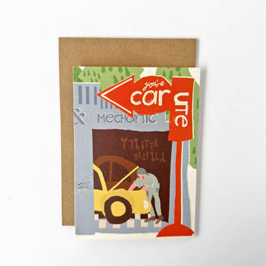 A greeting card with a brown kraft envelope, featuring a retro-style illustration of a mechanic working on a yellow car under a red sign that reads 'you're car-ute'.