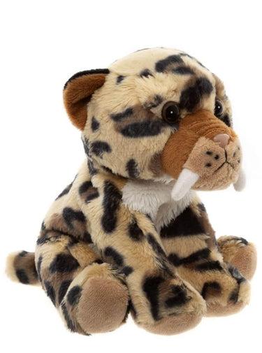 A plush toy of a saber-toothed cat with beige fur, black spots, brown ears and muzzle, and white tusks, photographed on a solid white background.