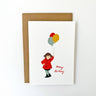 Greeting card with a child holding balloons and 'Happy Birthday' text, accompanied by a brown envelope on a white background.