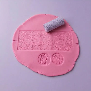 Pink play dough with embossed decorative motifs shown with a small purple roller on a light lavender background.