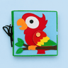 A square felt activity book featuring a colorful parrot design on a light blue background, with a green stitched border, black elastic closure, and button detail, shown on a light blue background.