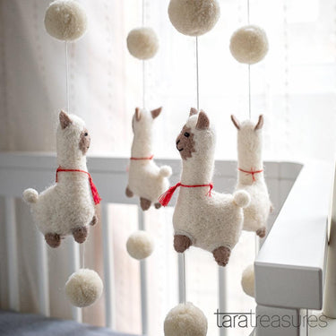 Decorative mobile with plush llamas and pom-poms hanging above a crib.