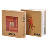 A brown box and a book with name Kapla with pink and orange wooden planks inside on a white background