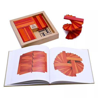 A brown box with pink and orange planks inside with a book showing a design and that design being made out of some other planks on a white background.