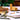 Green and yellow wooden planks being used to build structures on a white table with plants behind.