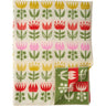 A folded knit blanket featuring a colorful tulip pattern on an off-white background, with a green corner tab showing the reverse side and stitching details.
