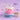 A pink birthday cake with white dripping frosting, a large purple number 2 candle, and two white spiral candles on a light blue stand. The scene is styled on a lavender background with callout labels pointing to the cake, stand, party dough, printed cake, number, and candle pack.