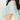 Close-up of a child wearing a pastel mint green tulle puff-sleeve top layered over a pale yellow dress, shown from the back against a plain white wall.
