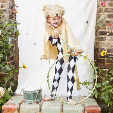 Child in a costume with a hula hoop, standing on a suitcase against a brick wall with plants.
