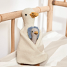 Knitted goose toy with a smaller toy inside, on a wooden crib.