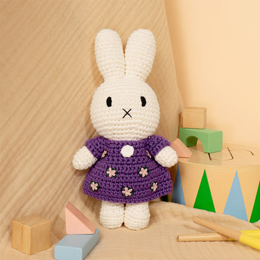 White crochet bunny toy in a purple dress with wooden blocks and toys on a wooden floor.