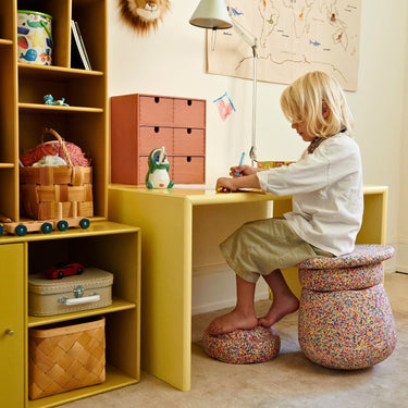 A child working at a desk using the Stapelstein Dynamic Sitting set. He sits on the seat and rests his feet  Australian a matching piece.