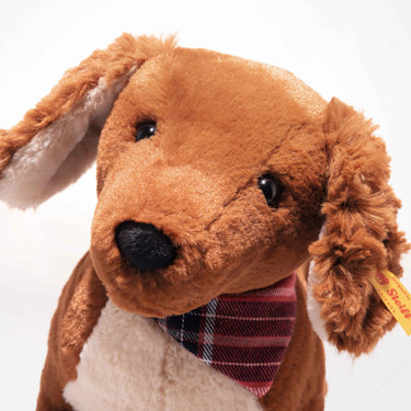 Close-up of a plush dachshund dog toy with a plaid bow tie on a white background
