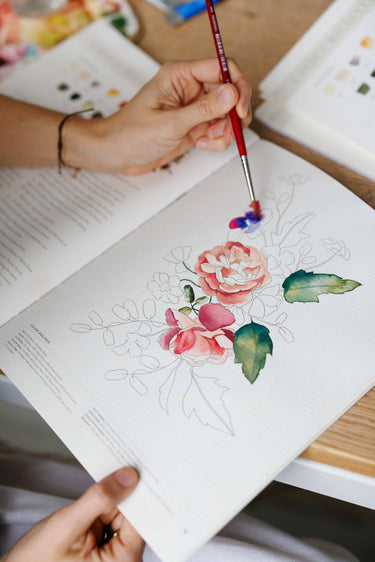 Person painting a floral design on paper with a brush